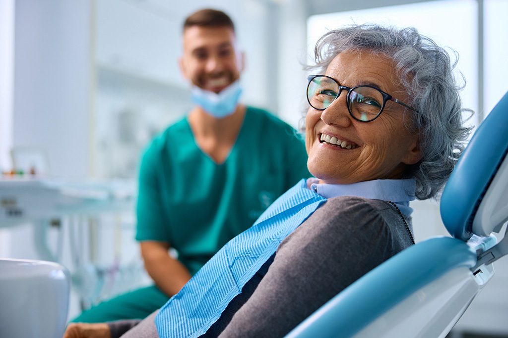 Older lady sitting in a dentist chair with a dentist besides her doing her routine dental checkup